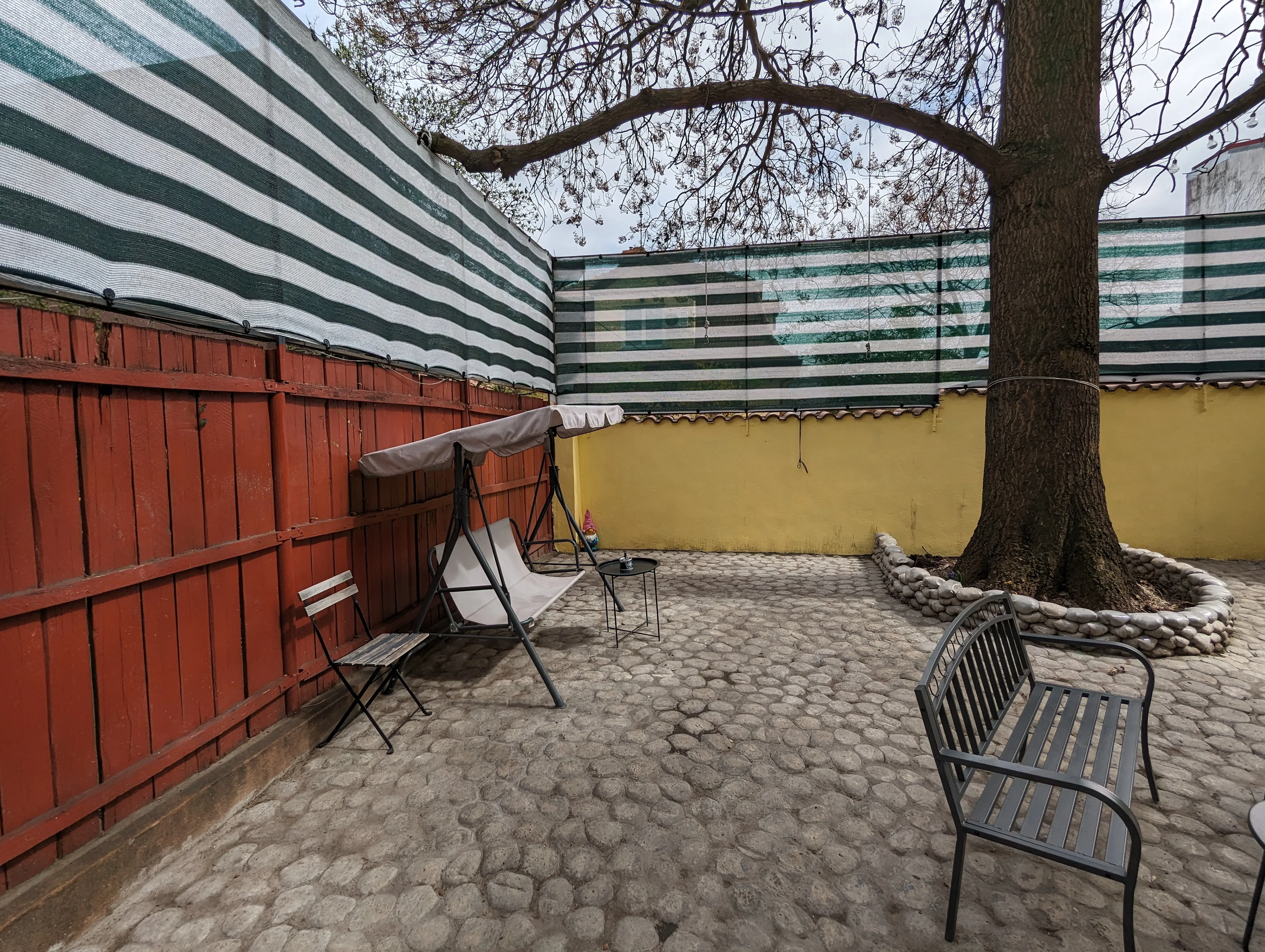 Coin de cour au Popcorn Hostel : palissade en bois rouge, balancelle à coussin blanc et pavage en galets de rivière.