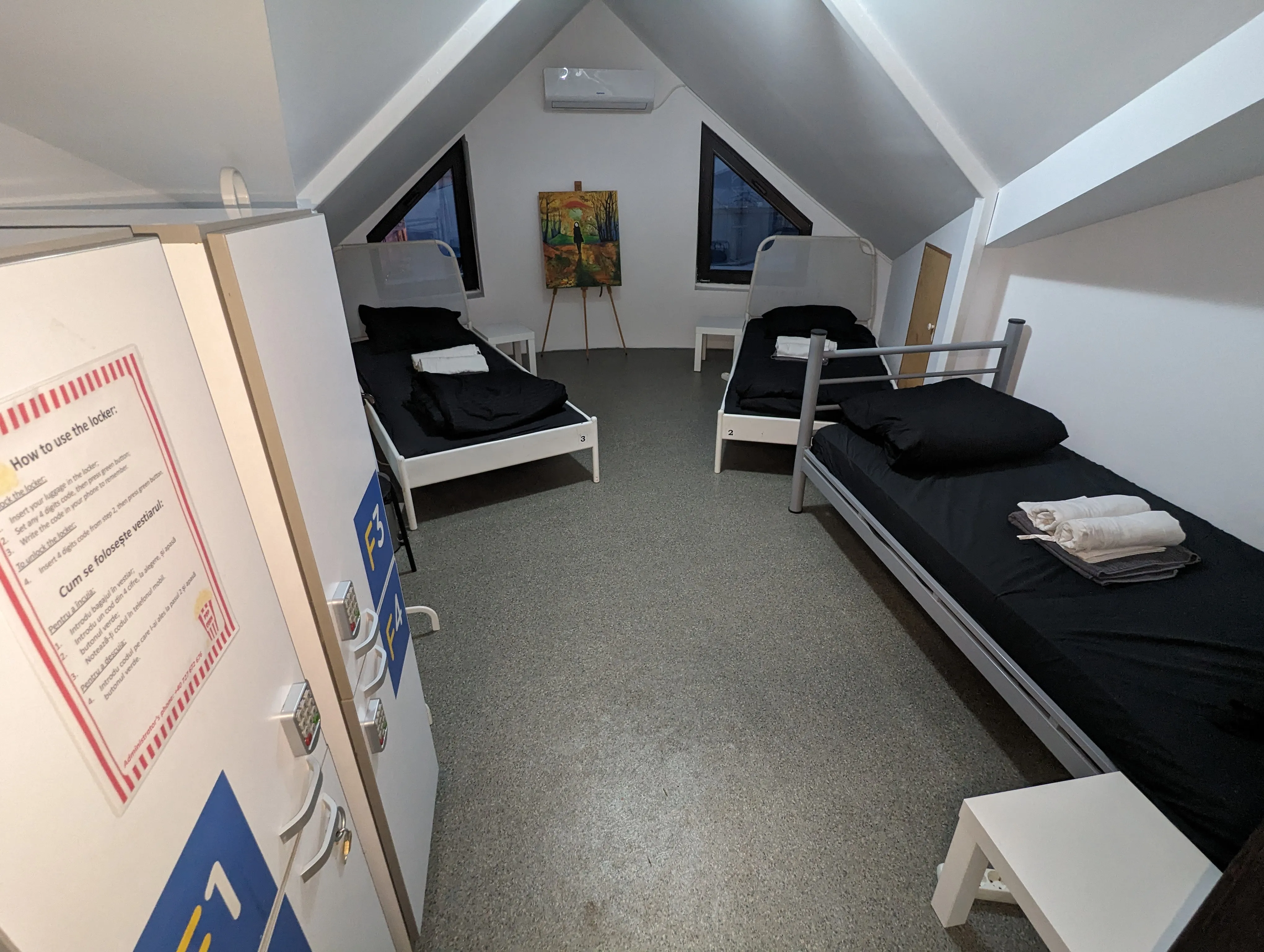 Dortoir 3 lits sous combles au Popcorn Hostel : murs blancs, climatisation et fenêtres de toit triangulaires.