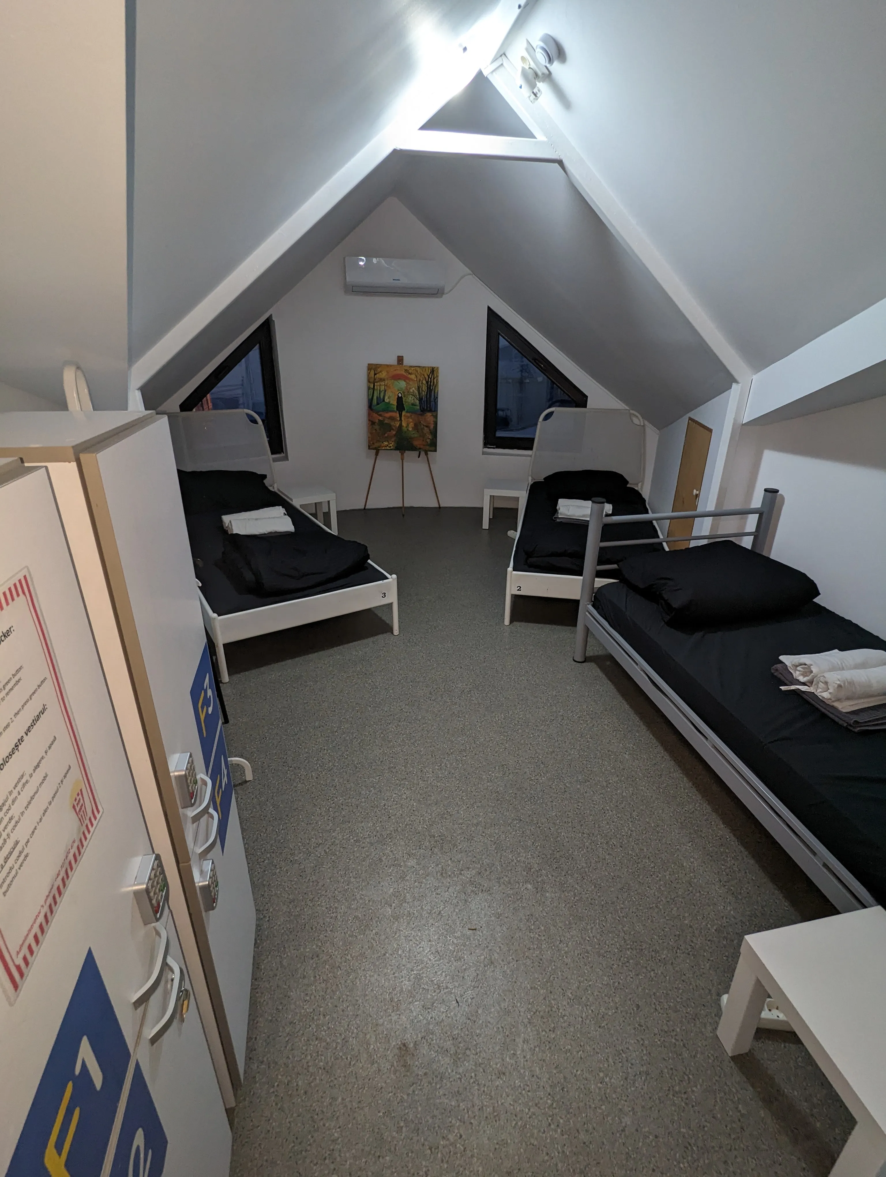 Dortoir 3 lits lumineux aux murs blancs et toile de coucher de soleil sur chevalet sous les combles du Popcorn Hostel.