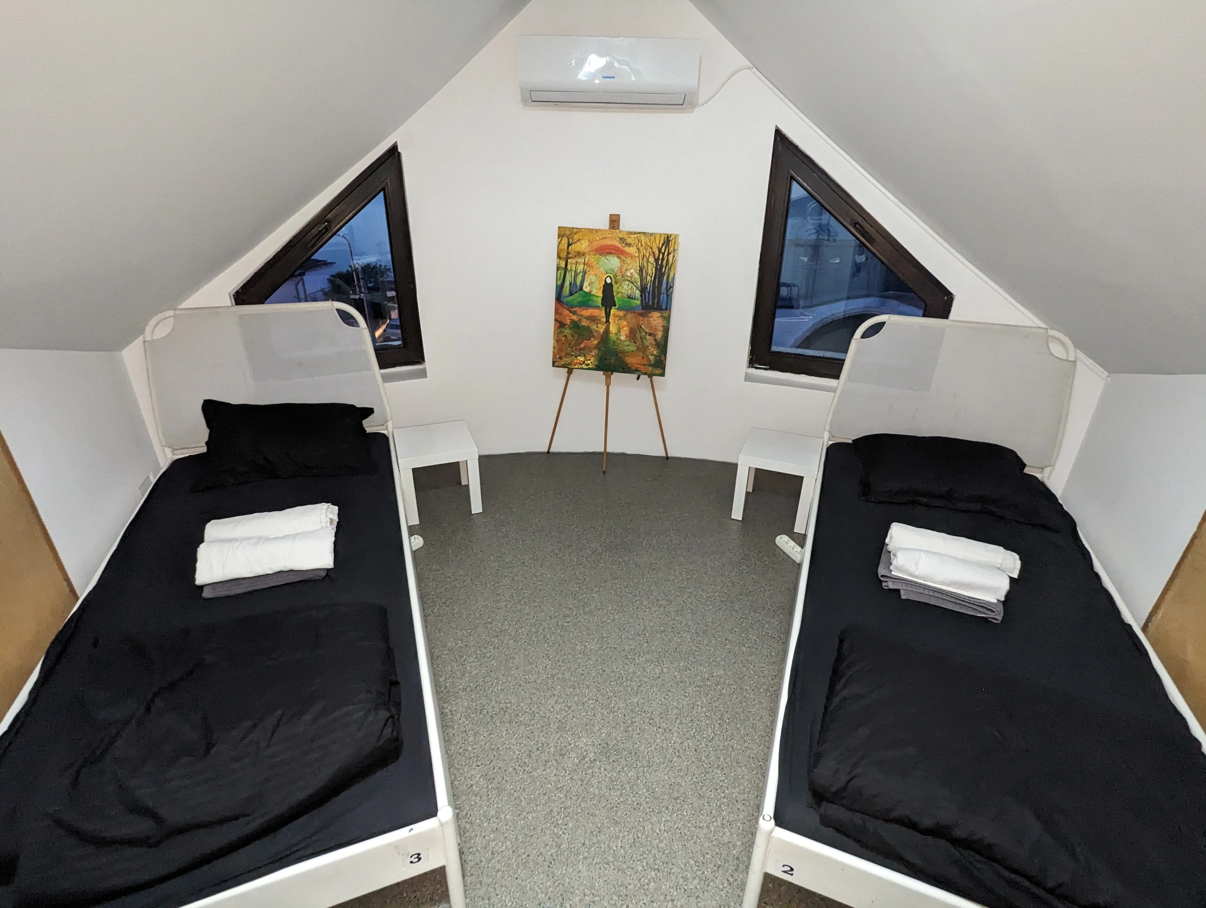 Deux lits simples symétriques avec serviettes pliées et une toile colorée de coucher de soleil entre eux au Popcorn Hostel.