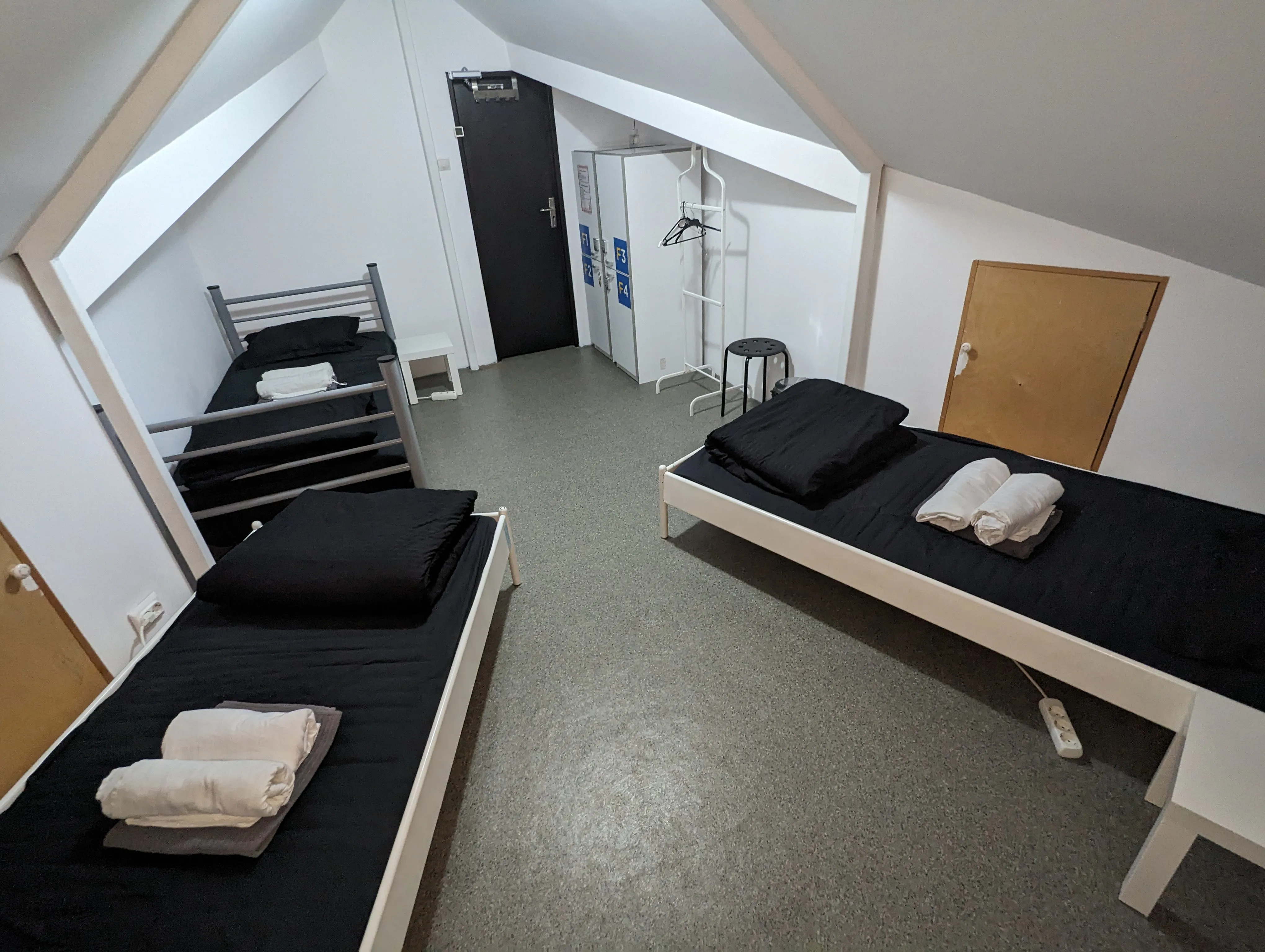 Dortoir 3 lits au Popcorn Hostel : coin penderie, miroir vertical et porte noire vers la salle de bain.