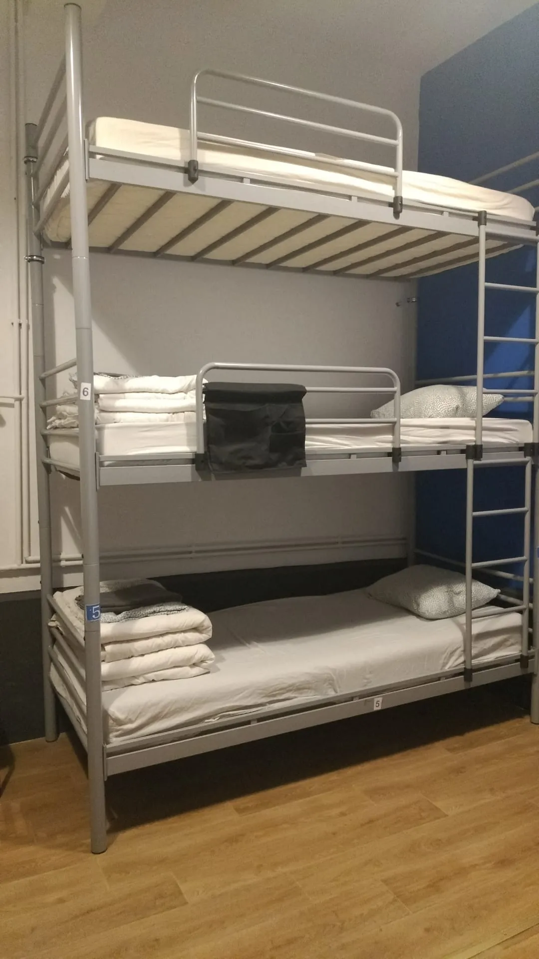 Popcorn Hostel ඇඳන් 9ක පොදු ඩෝමයේ නිල් accent බිත්තිය අසල මහල් 3ක bunk ඇඳන්.