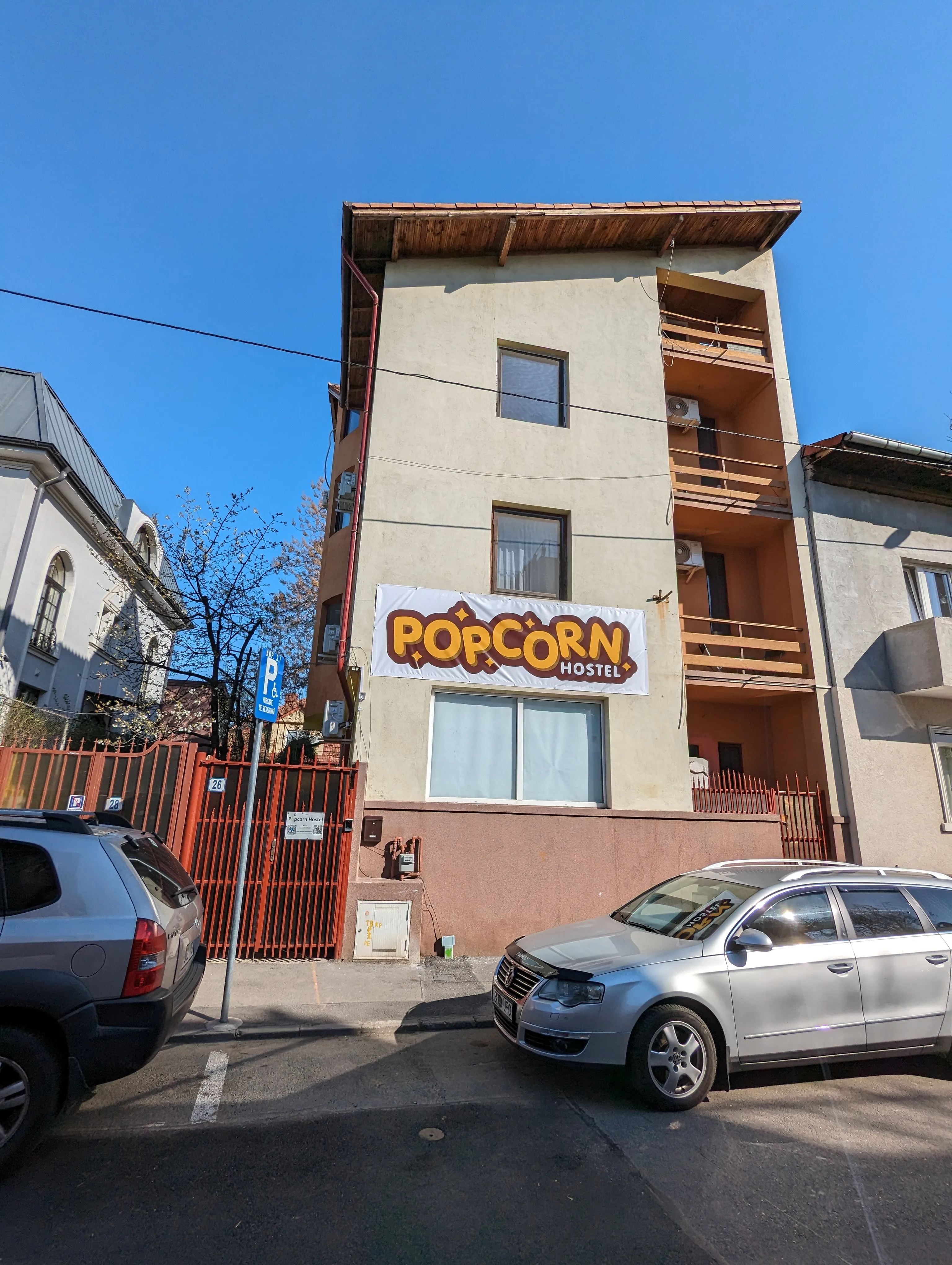 Façade du Popcorn Hostel rue Ing. Pisoni 26 à Bucarest, avec la banderole orange POPCORN HOSTEL au-dessus de l'entrée.