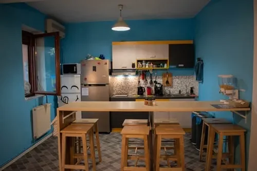 Cucina condivisa del Popcorn Hostel con pareti blu, frigo, piano cottura con cappa e lungo bancone in legno.