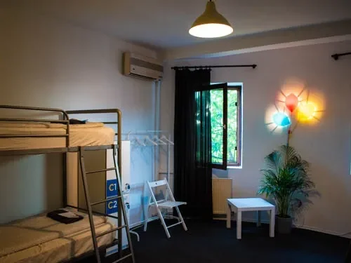 Camerata da 4 di giorno al Popcorn Hostel, con lampada a palloncini colorati e finestre aperte sul cortile.