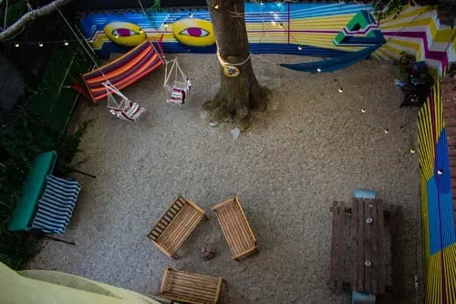 Vista dall'alto del cortile del Popcorn Hostel: albero centrale, amache, altalene e murales con occhi colorati.