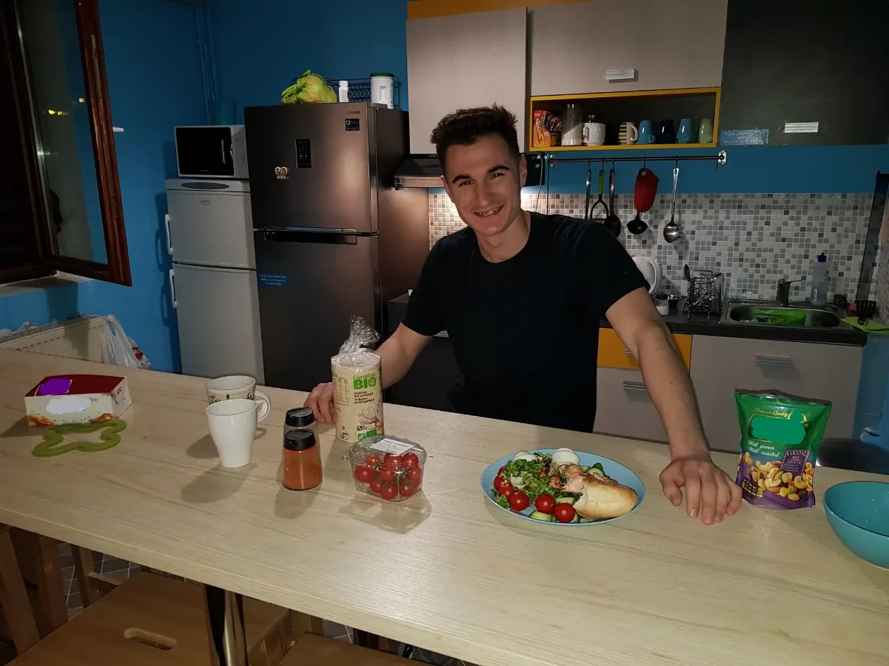 Ospite prepara la cena al bancone della cucina condivisa del Popcorn Hostel, con insalata fresca e pomodorini.