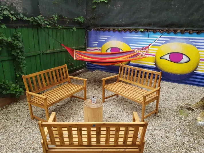 Tre panche di legno attorno a un ceppo e amaca a strisce sotto il murales con occhi nel cortile del Popcorn Hostel.