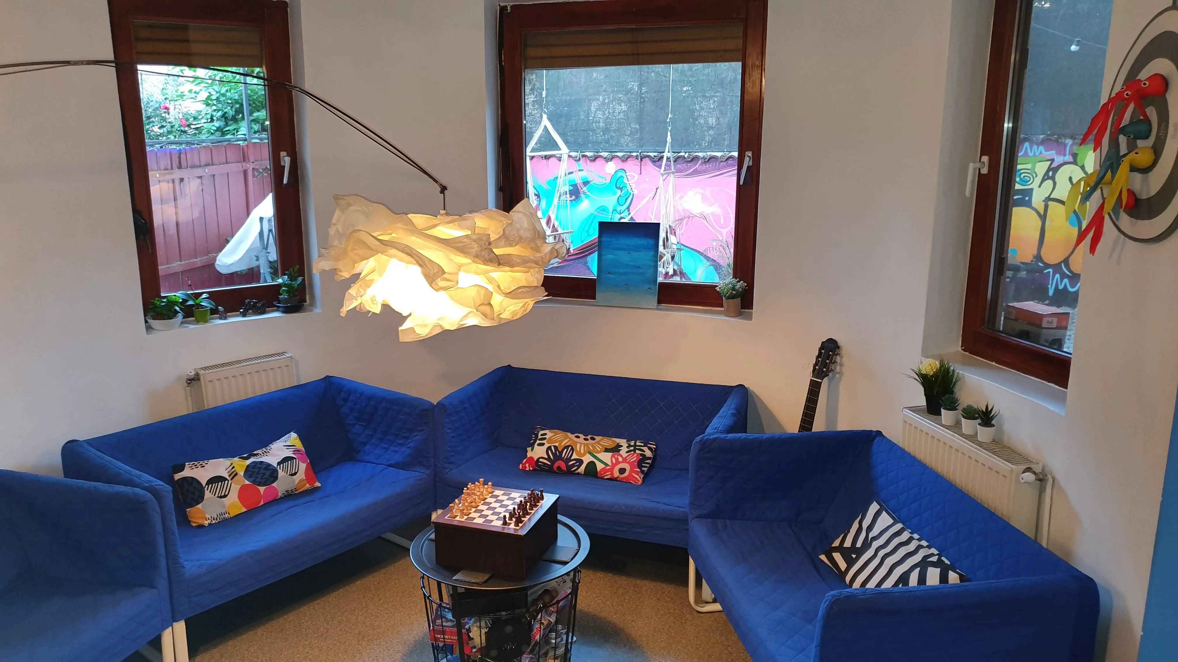 Trois canapés bleus en U avec coussins colorés et lampe suspendue dans le salon du Popcorn Hostel.